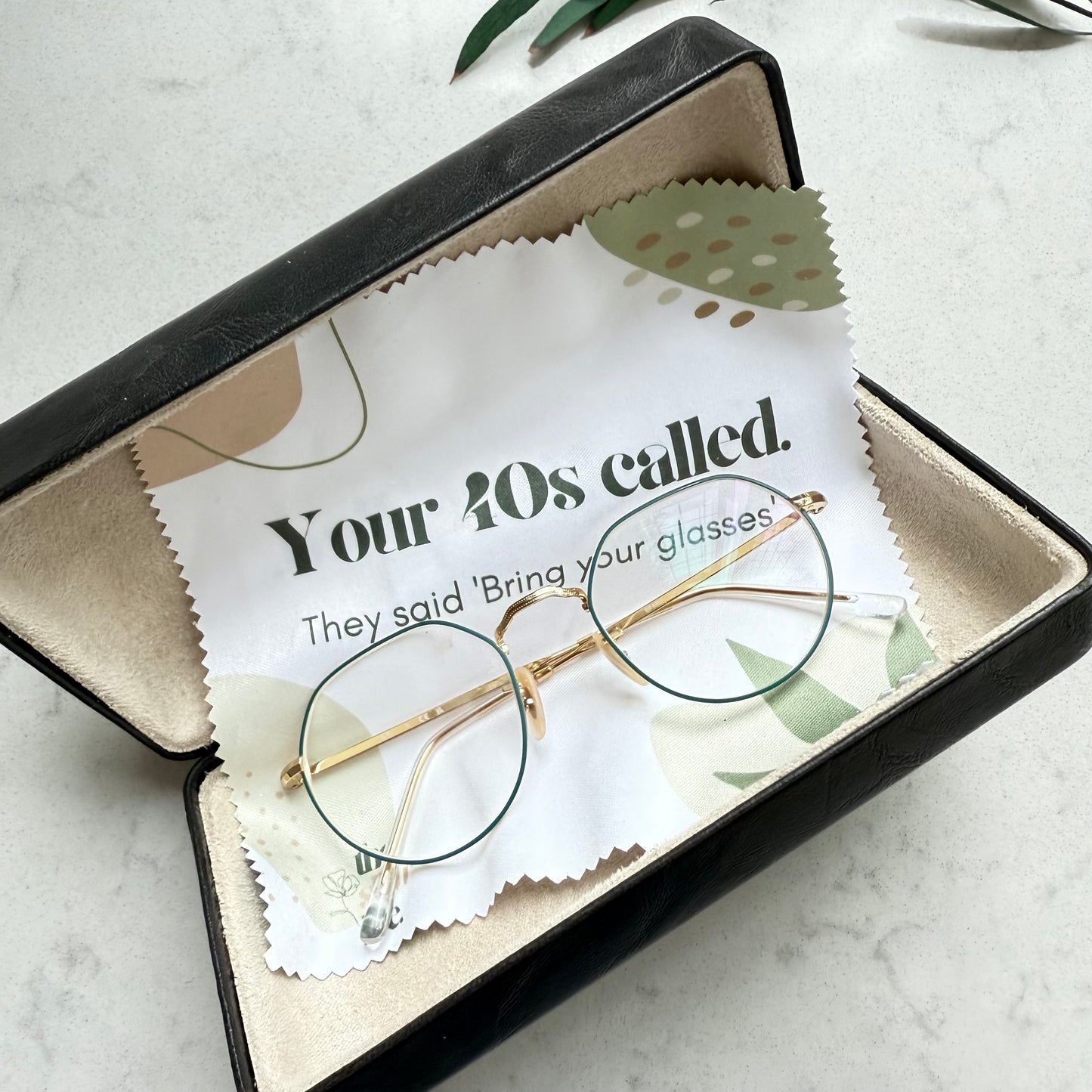 Gold-framed glasses in an open box with a message card on a light surface.
