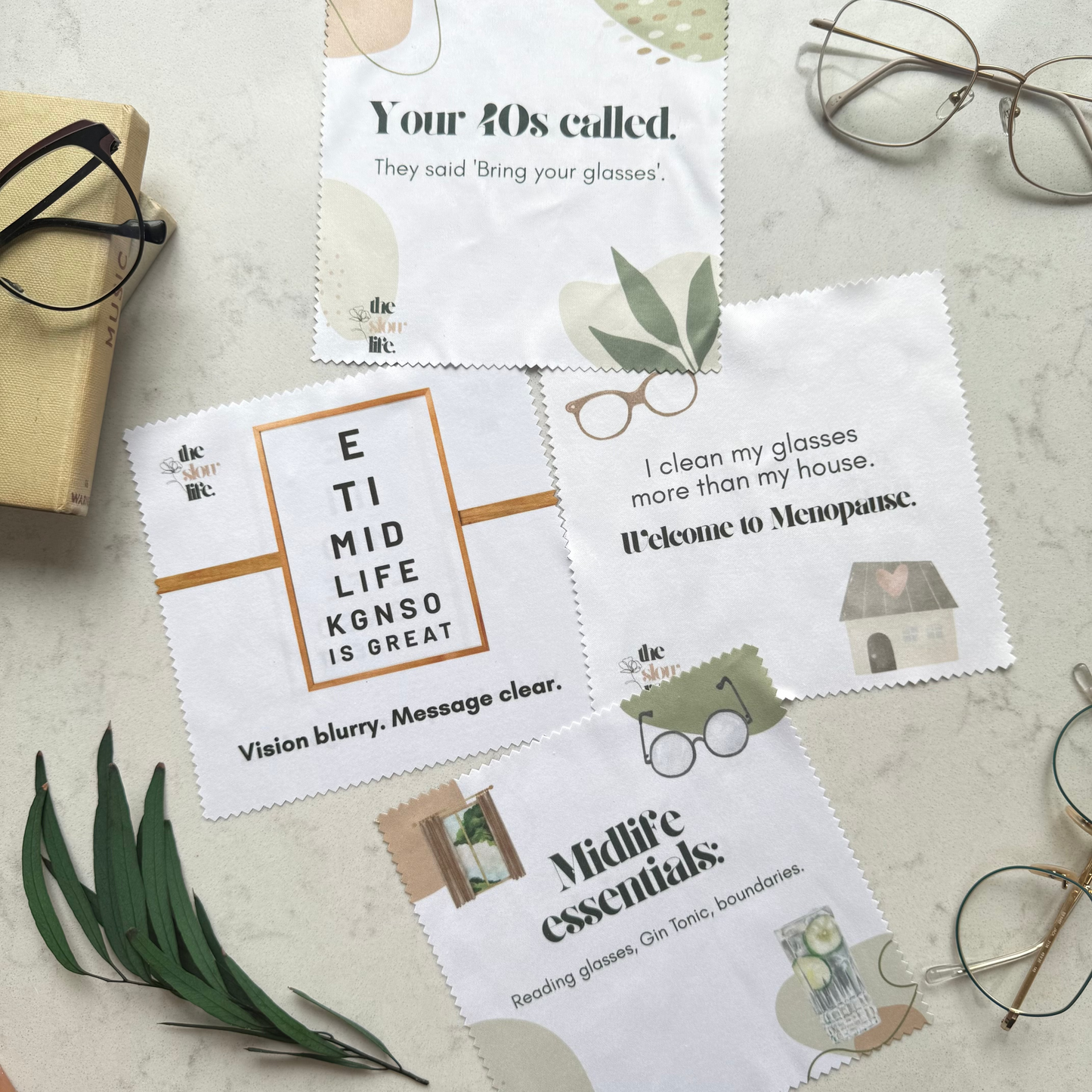Collection of eyeglass cleaning cloths with humorous text on a surface with glasses and leaves.