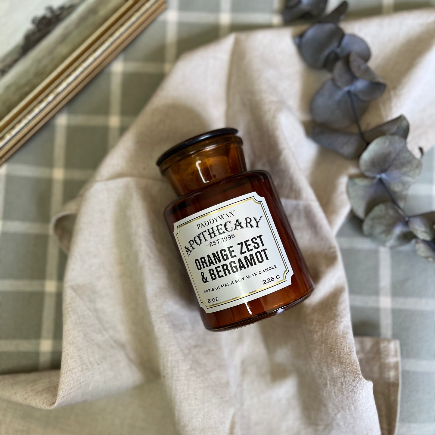 Apothecary Glass Jar Candle in Orange Zest & Bergamot scent, elegantly placed on a wooden table with surrounding rustic decor elements, creating a cozy ambiance.