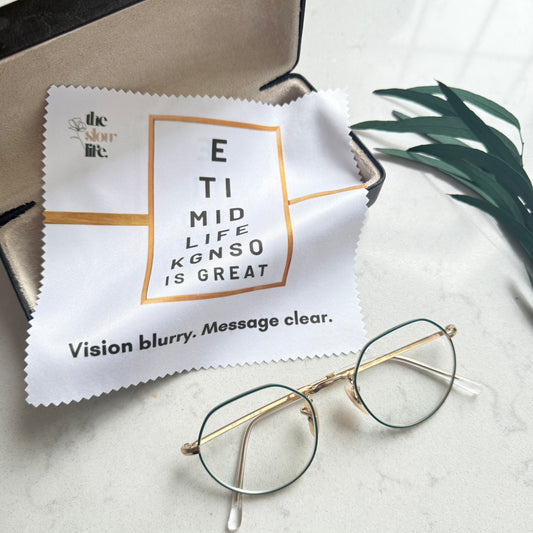 Eyeglasses and a cleaning cloth with humorous text on a light surface.