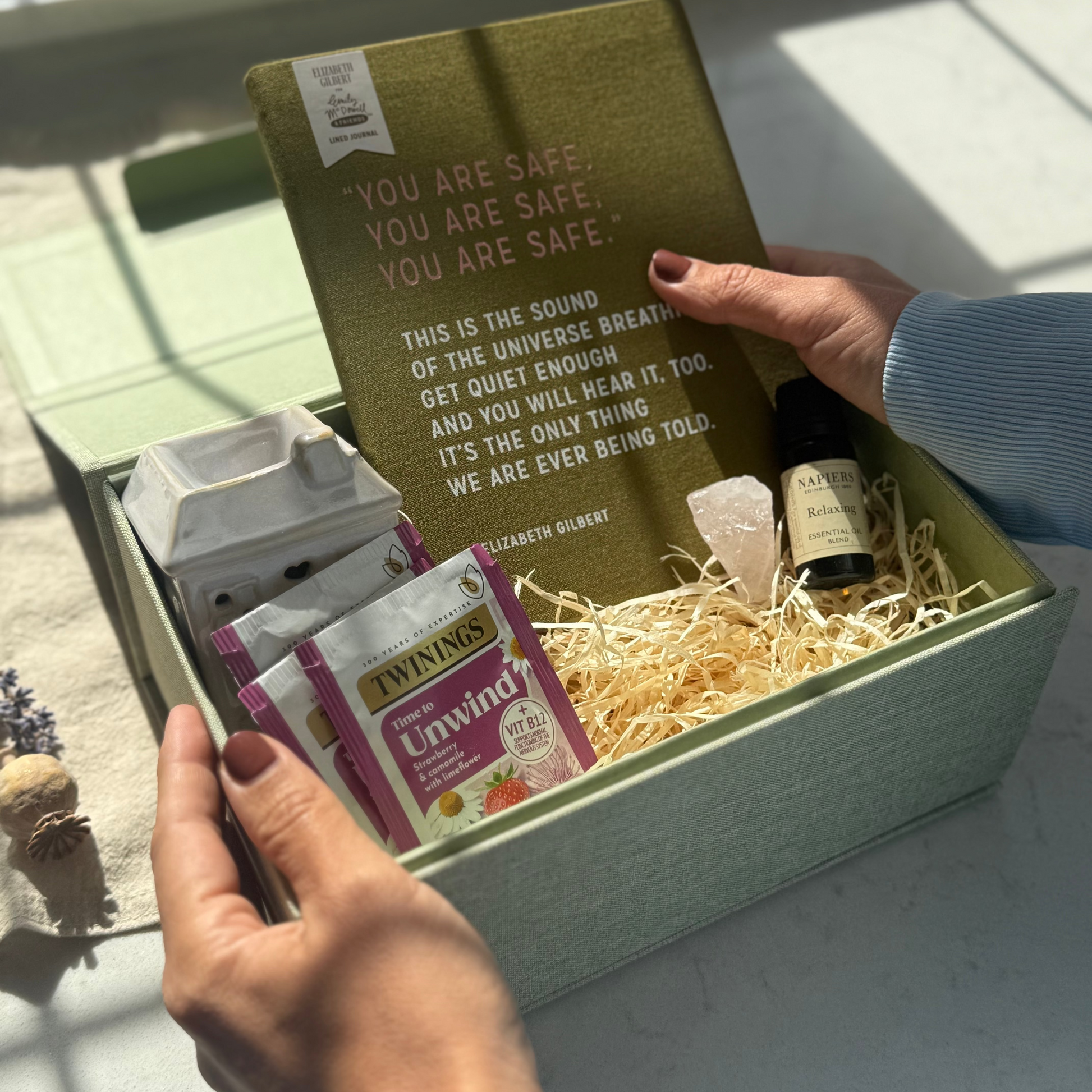 Gift box with a book, tea bags, and a bottle, held by a hand.