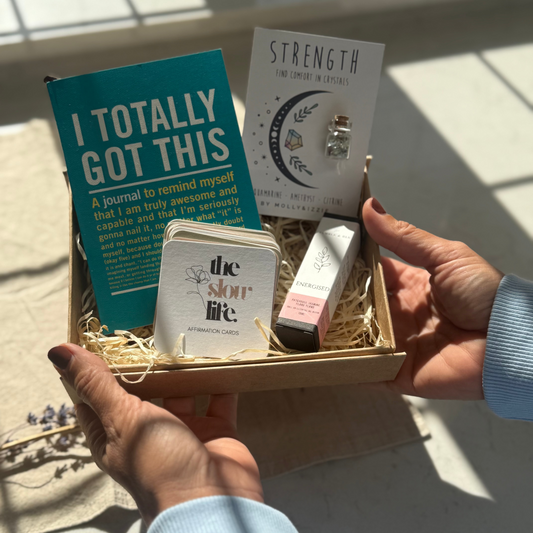 Hand holding a gift box with 'I Totally Got This' book, 'Strength' card, and other items.