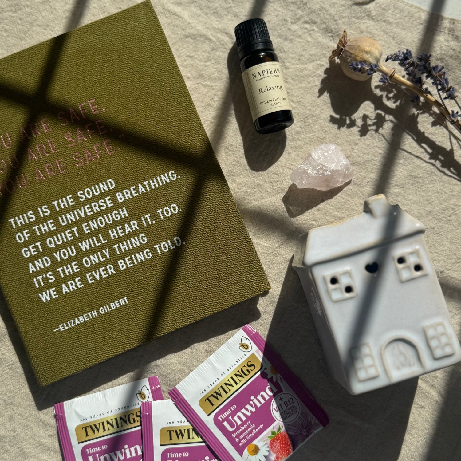 Relaxation items including a book, essential oil bottle, crystal, and tea packages on a textured surface.