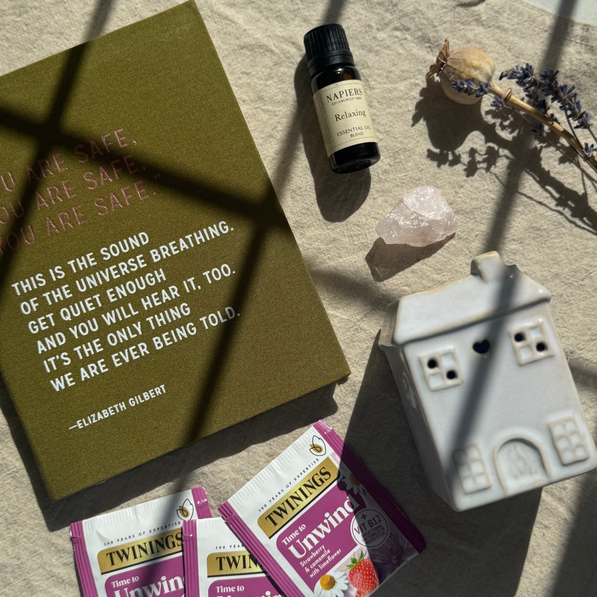 Relaxation items including a book, essential oil bottle, crystal, and tea packages on a textured surface.