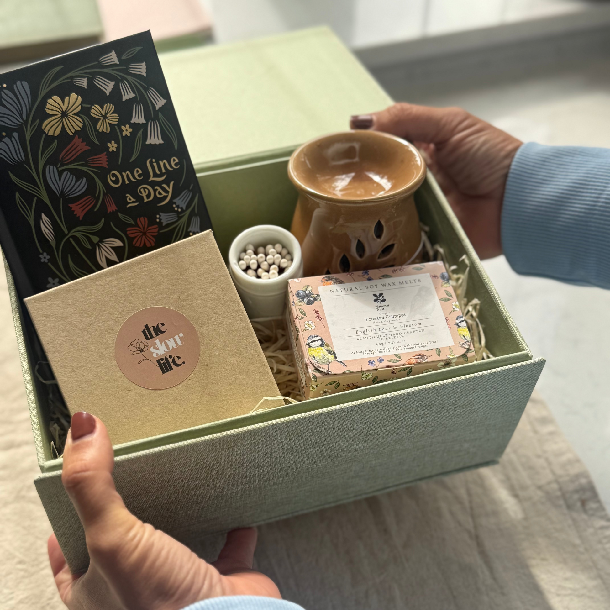 Hand holding a gift box with various items including a mug and books.