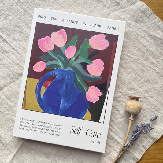 Booklet titled 'Self-Care' with a blue vase and pink tulips on a textured surface.