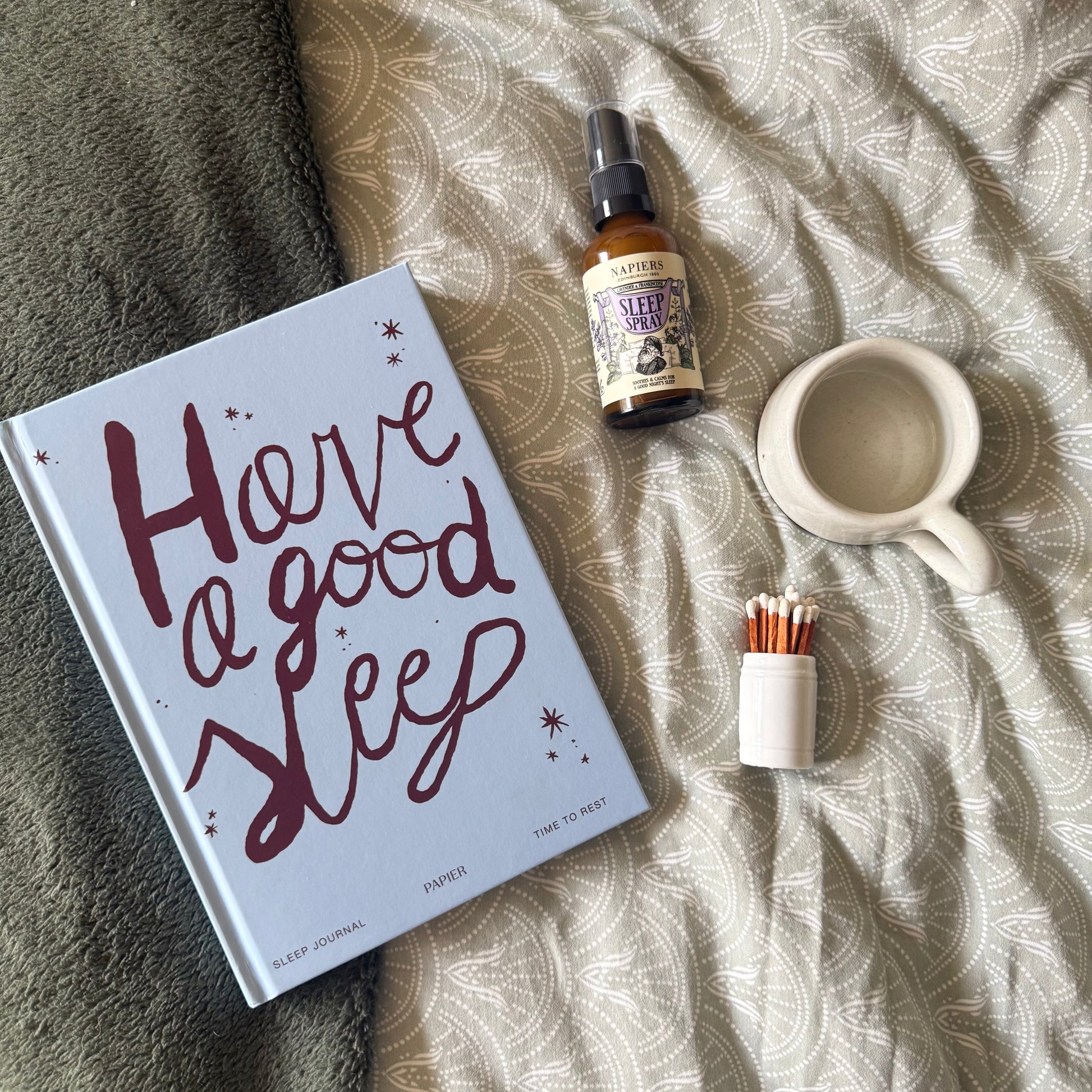 Sleep journal with 'Have a good sleep' text, sleep spray, and mug on patterned fabric