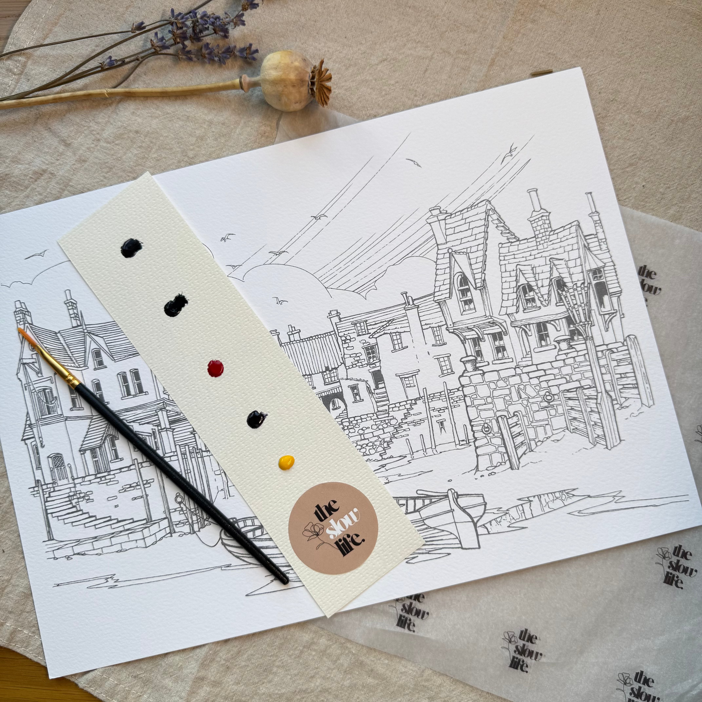 Artistic drawing of a building on paper with a paint palette and brush on a textured surface.