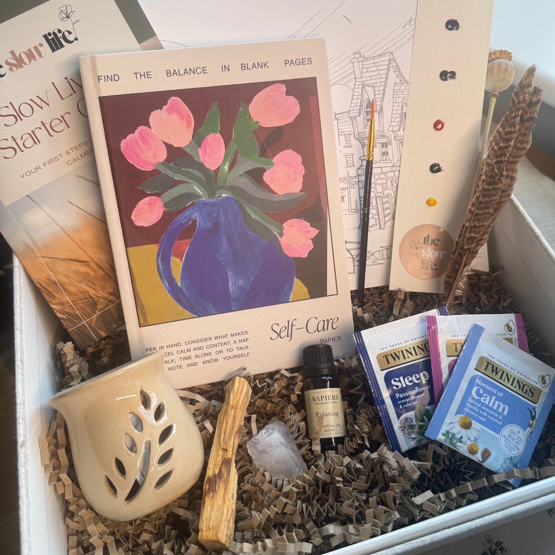 Box containing self-care items including a book, candles, and wellness products.