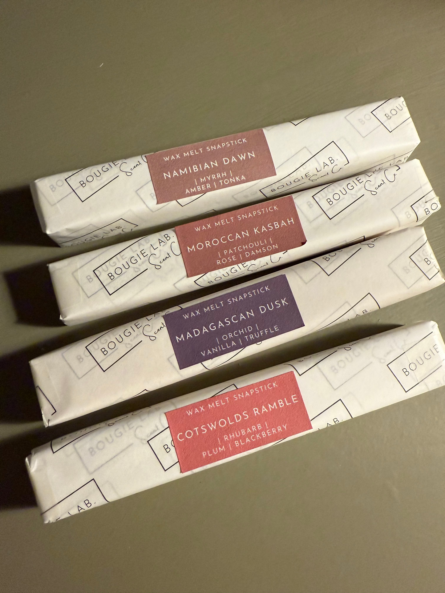 Five wax melt sticks in their packaging with labels on a neutral background