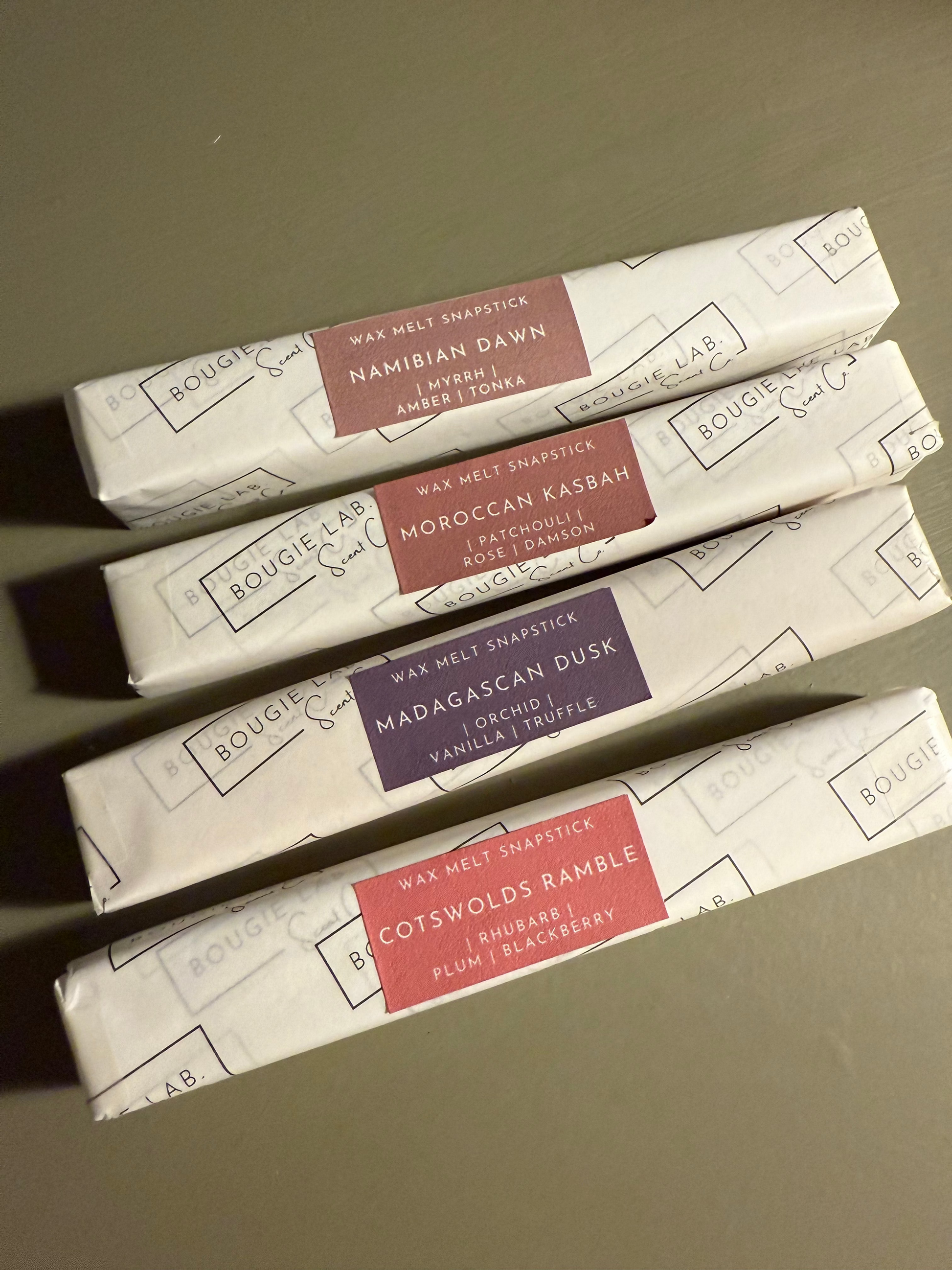 Five wax melt sticks in their packaging with labels on a neutral background