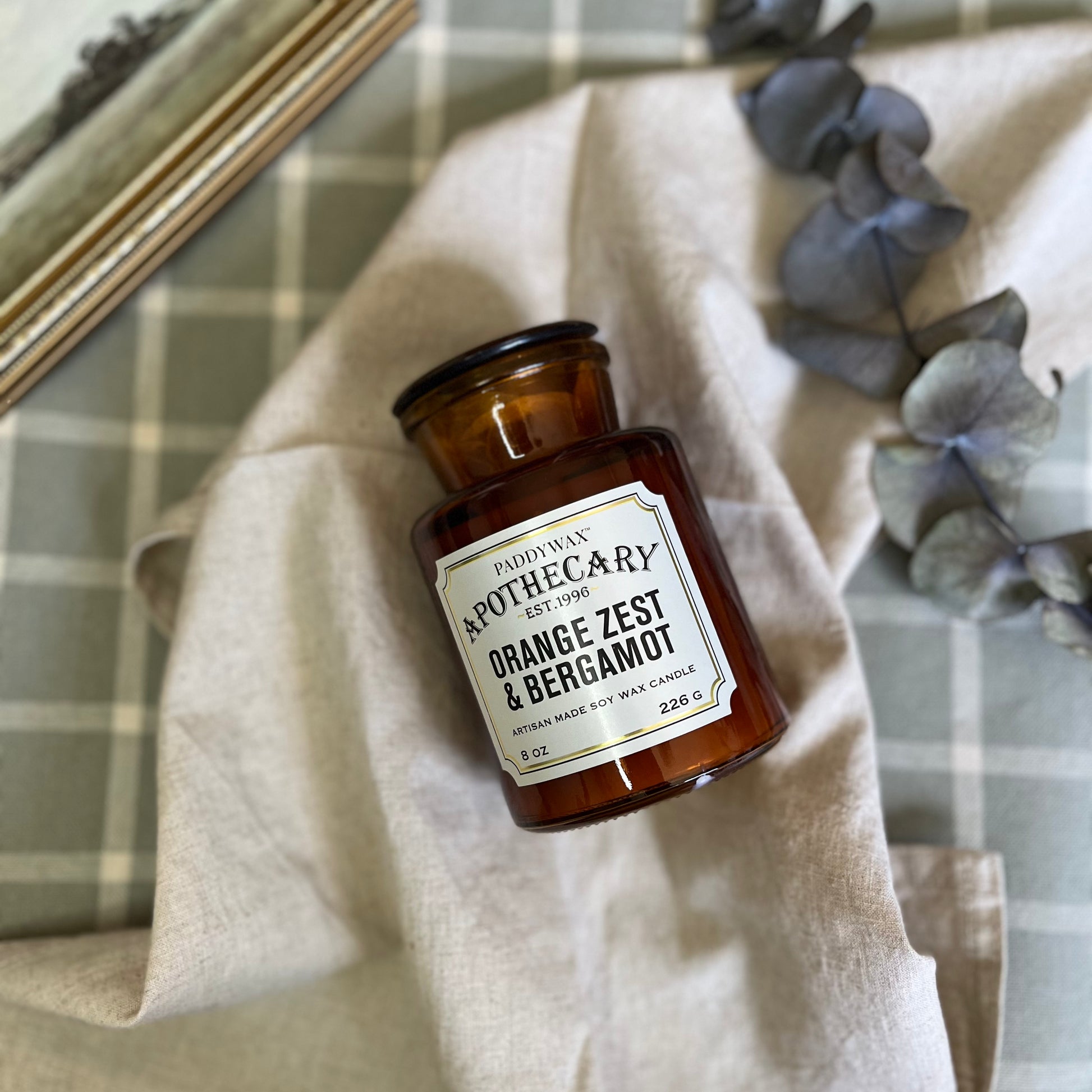 Apothecary Glass Jar Candle in Orange Zest & Bergamot scent, elegantly placed on a wooden table with surrounding rustic decor elements, creating a cozy ambiance.